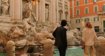Movie still from “To Rome with Love” (2012), directed by Woody Allen – A man standing in front of a fountain in front of a building; Wide shot, Over the shoulder angle