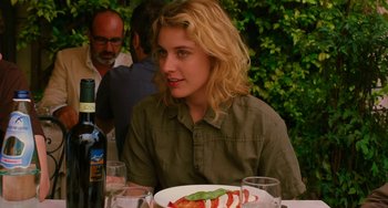 Movie still from “To Rome with Love” (2012), directed by Woody Allen – A woman sitting at a table with a plate of food on top of it; Close Up shot, Over the shoulder angle