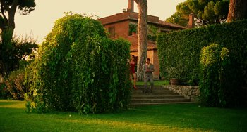 Movie still from “To Rome with Love” (2012), directed by Woody Allen – A couple of people standing next to a tree in front of a house; Extreme Wide shot, Low angle
