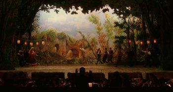 Movie still from “To Rome with Love” (2012), directed by Woody Allen – People sitting in front of a painting on a stage; Extreme Wide shot, High angle