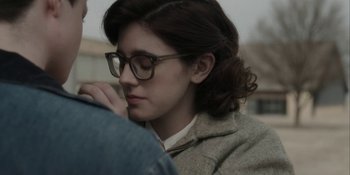 Movie still from “To the Stars” (2019), directed by Martha Stephens – A young woman wearing glasses and a jacket; Close Up shot, Over the shoulder angle