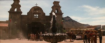 Movie still from “Tombstone” (1993), directed by George P. Cosmatos – A fountain in front of an old building with a horse and carriage in front of it; Extreme Wide shot, Low angle