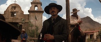 Movie still from “Tombstone” (1993), directed by George P. Cosmatos – A man in a black hat is standing in front of a building; Medium shot, Low angle