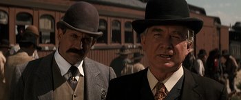 Movie still from “Tombstone” (1993), directed by George P. Cosmatos – Two men in suits and hats standing next to each other in front of a building; Close Up shot, Low angle