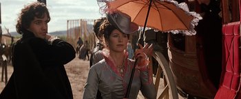 Movie still from “Tombstone” (1993), directed by George P. Cosmatos – A woman holding an umbrella while standing in a field; Medium shot, Low angle