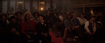 Movie still from “Tombstone” (1993), directed by George P. Cosmatos – A group of people sitting in a room; Wide shot, Low angle