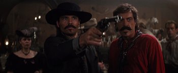Movie still from “Tombstone” (1993), directed by George P. Cosmatos – A man in a black hat holding a gun pointed at the camera; Close Up shot, Low angle