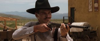 Movie still from “Tombstone” (1993), directed by George P. Cosmatos – A man in a cowboy hat holding a gun; Close Up shot, Low angle