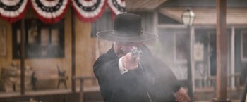 Movie still from “Tombstone” (1993), directed by George P. Cosmatos – A man in a black suit and a black hat is holding a gun; Medium shot, Low angle