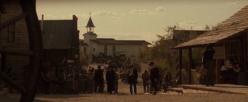 Movie still from “Tombstone” (1993), directed by George P. Cosmatos – A group of people standing on a dirt road near a church; Extreme Wide shot, Low angle