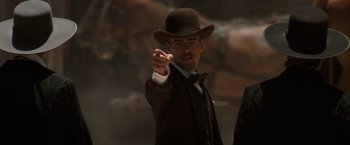 Movie still from “Tombstone” (1993), directed by George P. Cosmatos – A man wearing a hat and a suit points to the side; Medium shot, Low angle