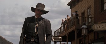 Movie still from “Tombstone” (1993), directed by George P. Cosmatos – A man in a suit and hat standing in front of people; Medium shot, Low angle