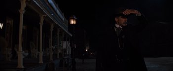 Movie still from “Tombstone” (1993), directed by George P. Cosmatos – A man in a suit and hat standing next to a street light; Medium shot, Low angle