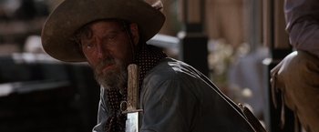 Movie still from “Tombstone” (1993), directed by George P. Cosmatos – A man in a cowboy hat holding a gun in his hand; Close Up shot, Over the shoulder angle
