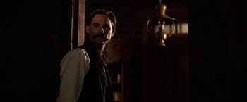 Movie still from “Tombstone” (1993), directed by George P. Cosmatos – A man with a mustache standing next to a lamp; Medium shot, Over the shoulder angle