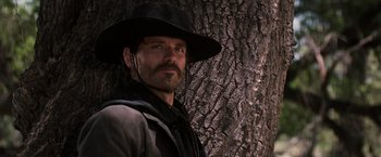 Movie still from “Tombstone” (1993), directed by George P. Cosmatos – A man in a black hat standing in front of a tree; Close Up shot, Low angle