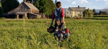 Movie still from “Tomorrowland” (2015), directed by Brad Bird – A young boy walking through a field with a baseball glove and a bag; Wide shot, High angle