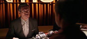 Movie still from “Tomorrowland” (2015), directed by Brad Bird – A man sitting at a table with a camera in front of him; Close Up shot, Over the shoulder angle