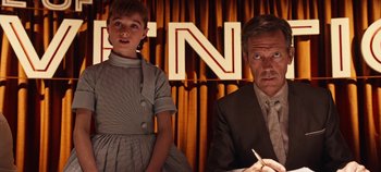 Movie still from “Tomorrowland” (2015), directed by Brad Bird – A man and a woman sitting next to each other in front of a curtain; Medium shot, Over the shoulder angle