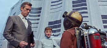 Movie still from “Tomorrowland” (2015), directed by Brad Bird – A group of people standing next to each other in front of a wall; Medium shot, Over the shoulder angle