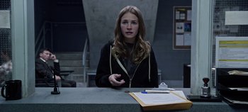 Movie still from “Tomorrowland” (2015), directed by Brad Bird – A woman sitting at a table in front of a clipboard; Medium shot, Over the shoulder angle