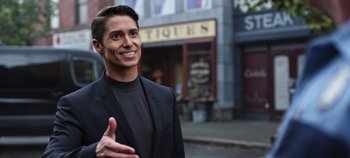 Movie still from “Tomorrowland” (2015), directed by Brad Bird – A man in a black suit is smiling and holding his hand out; Medium shot, Over the shoulder angle