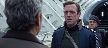 Movie still from “Tomorrowland” (2015), directed by Brad Bird – A man in a black jacket talking to another man in a black jacket; Close Up shot, Over the shoulder angle