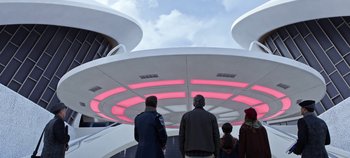Movie still from “Tomorrowland” (2015), directed by Brad Bird – A group of people standing under a building with lights; Wide shot, Low angle