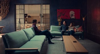 Movie still from “Too Old to Die Young” (2019), directed by Nicolas Winding Refn – A group of people sitting in a living room on couches; Wide shot, High angle