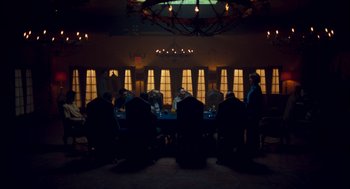 Movie still from “Too Old to Die Young” (2019), directed by Nicolas Winding Refn – A group of people sitting at a table in front of a window; Wide shot, Low angle