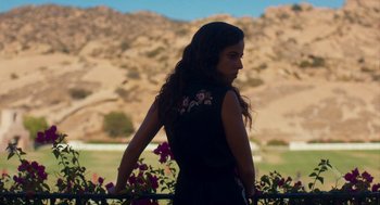 Movie still from “Too Old to Die Young” (2019), directed by Nicolas Winding Refn – A woman standing in front of a fence with flowers; Medium shot, Low angle