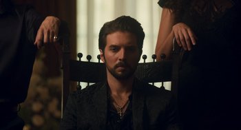 Movie still from “Too Old to Die Young” (2019), directed by Nicolas Winding Refn – A man sitting in a chair in front of a woman; Medium shot, Low angle