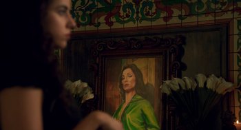 Movie still from “Too Old to Die Young” (2019), directed by Nicolas Winding Refn – A woman standing in front of a painting of a woman; Close Up shot, Over the shoulder angle
