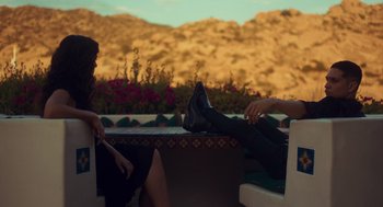 Movie still from “Too Old to Die Young” (2019), directed by Nicolas Winding Refn – Two people sitting on a bench with their feet on the ground; Wide shot, High angle