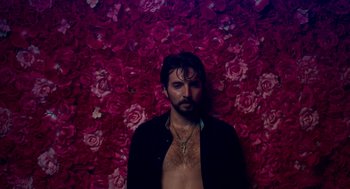 Movie still from “Too Old to Die Young” (2019), directed by Nicolas Winding Refn – A man standing in front of a wall of flowers; Medium shot, High angle