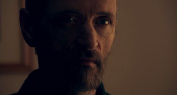 Movie still from “Too Old to Die Young” (2019), directed by Nicolas Winding Refn – A person with a beard looking at the camera; Close Up shot, Low angle