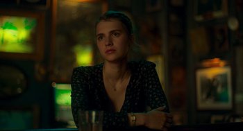 Movie still from “Too Old to Die Young” (2019), directed by Nicolas Winding Refn – A woman sitting at a table in front of a glass of water; Close Up shot, Over the shoulder angle