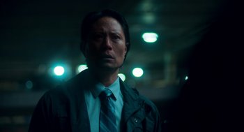 Movie still from “Too Old to Die Young” (2019), directed by Nicolas Winding Refn – A man wearing a suit and tie in a dimly - lit room; Close Up shot, Low angle