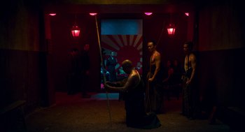 Movie still from “Too Old to Die Young” (2019), directed by Nicolas Winding Refn – A man is holding a spear in front of other men; Wide shot, Over the shoulder angle