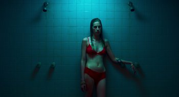 Movie still from “Too Old to Die Young” (2019), directed by Nicolas Winding Refn – A woman in a red bathing suit standing in a shower; Medium shot, Overhead angle