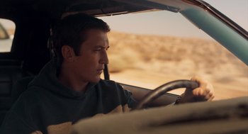 Movie still from “Too Old to Die Young” (2019), directed by Nicolas Winding Refn – A man sitting in the driver's seat of a car driving down a desert road; Close Up shot, Low angle