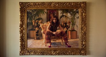 Movie still from “Too Old to Die Young” (2019), directed by Nicolas Winding Refn – A woman sitting on a chair in a room with plants; Wide shot, Low angle