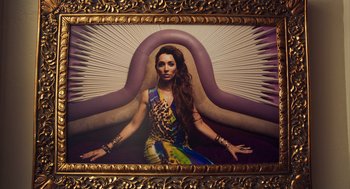 Movie still from “Too Old to Die Young” (2019), directed by Nicolas Winding Refn – A woman sitting in front of an image in a gold frame; Medium shot, Overhead angle