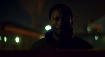 Movie still from “Too Old to Die Young” (2019), directed by Nicolas Winding Refn – A man in a black jacket standing in the dark; Close Up shot, Low angle