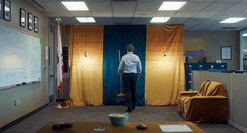 Movie still from “Too Old to Die Young” (2019), directed by Nicolas Winding Refn – A man holding a mop in a room with curtains; Wide shot, High angle