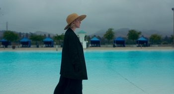 Movie still from “Too Old to Die Young” (2019), directed by Nicolas Winding Refn – A woman wearing a hat standing in front of a pool; Wide shot, High angle