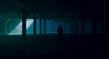 Movie still from “Too Old to Die Young” (2019), directed by Nicolas Winding Refn – A person walking in a dark room at night; Extreme Wide shot, Low angle