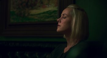 Movie still from “Too Old to Die Young” (2019), directed by Nicolas Winding Refn – A woman sitting in front of a painting with her eyes closed; Close Up shot, Low angle