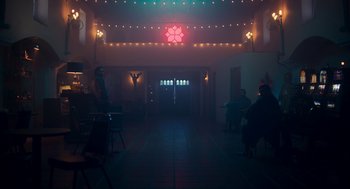 Movie still from “Too Old to Die Young” (2019), directed by Nicolas Winding Refn – People sitting at tables in a dark room with lights; Extreme Wide shot, Low angle