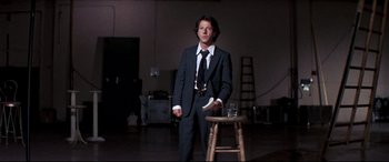 Movie still from “Tootsie” (1982), directed by Sydney Pollack – A man in a suit and tie standing next to a wooden stool; Medium shot, Low angle